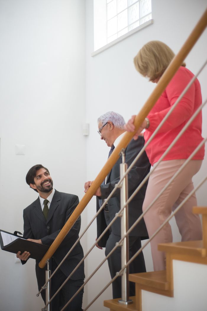 Realtor showing a house to an elderly couple on stairs, engaging in discussion.